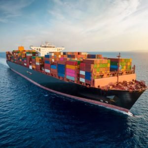 Aerial view of a large, loaded container cargo ship traveling over open ocean during sunset time